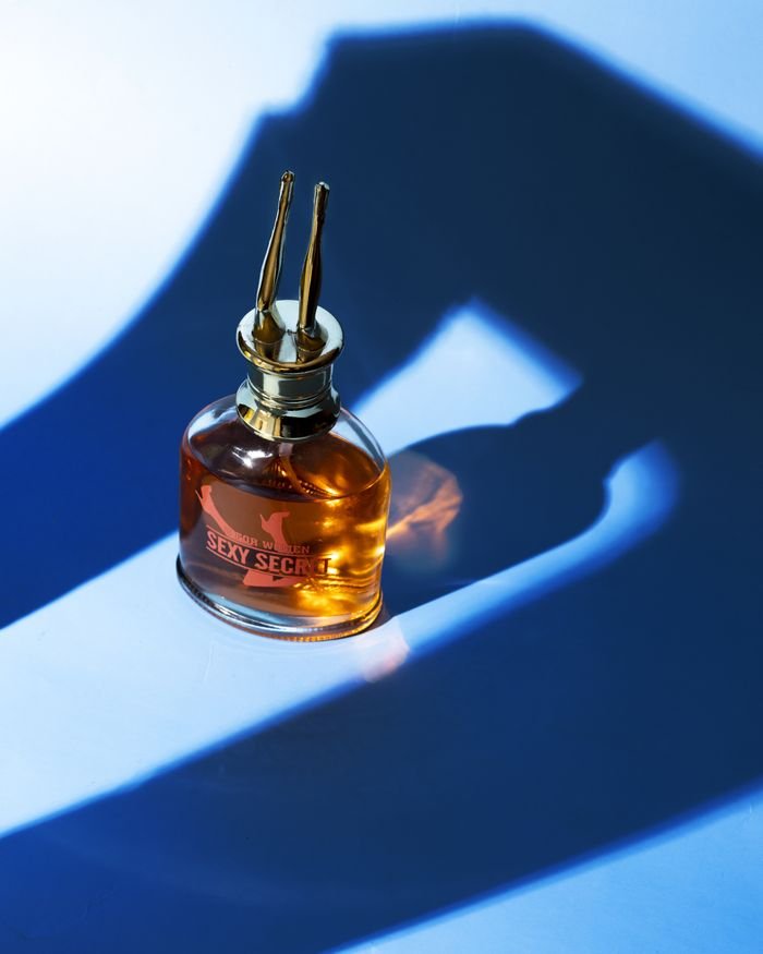 A stylish perfume bottle with golden accents casting a unique shadow on a blue background.